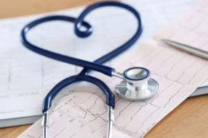 Medizinisches Stethoskop in Herzform verdreht auf Kardiogrammkarte liegend in Nahaufnahme.
